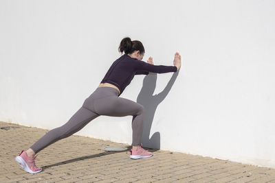 Sporty woman pushing against a white wall, warm up exercises.