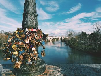 Statue of padlocks on bridge over river against sky