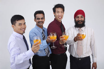 Portrait of smiling businessmen holding orange juice against white background