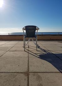 Empty chair on beach against sky on sunny day