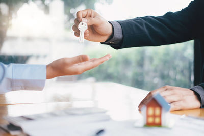 Cropped hand of businessman giving house keys to customer in office