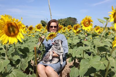 Portrait of smiling woman holding sunflower against yellow flowering plants