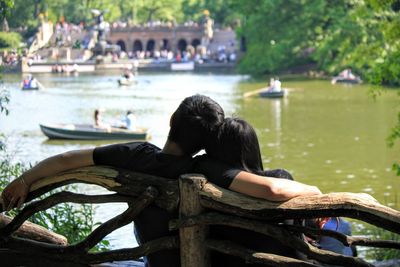 Rear view of couple sitting on bench at riverbank