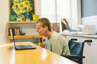 Handsome young invalid disabled man talking on mobile phone in kittchen. person with disabilities
