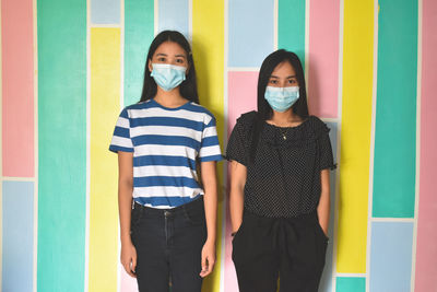 Portrait of two young adult standing against wall