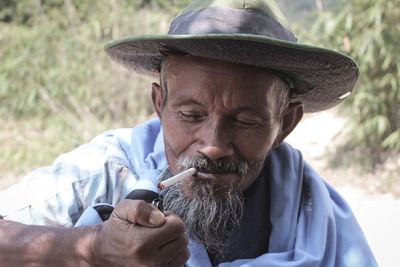 Mature man wearing hat igniting cigarette with lighter