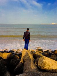 Rear view of man standing on concrete block against sea at beach