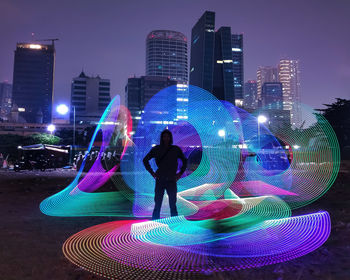 Woman standing by illuminated modern buildings in city at night