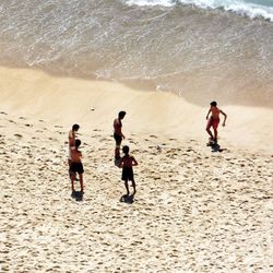 High angle view of shirtless boys playing soccer on sandy beach during sunny day