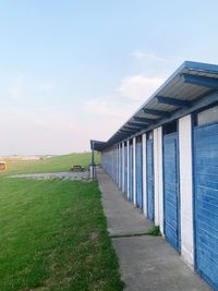 Empty footpath amidst field against sky