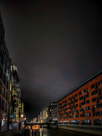 Illuminated buildings by street against sky at night