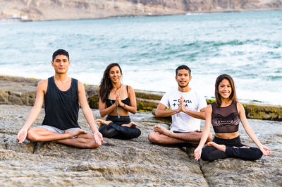 Portrait of friends doing yoga on rock at beach