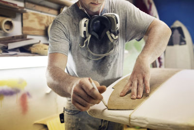 Midsection of man preparing surfboard in workshop