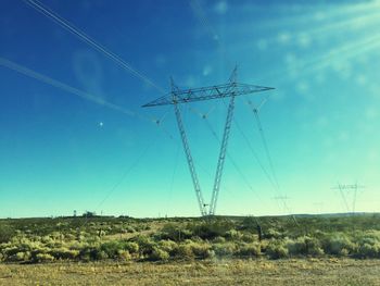 Low angle view of electricity pylon on field against blue sky