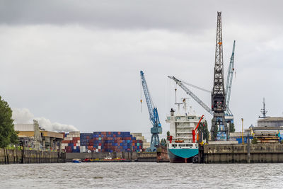 Cranes at harbor against sky