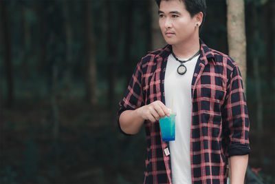 Man holding blue drink while looking away in forest