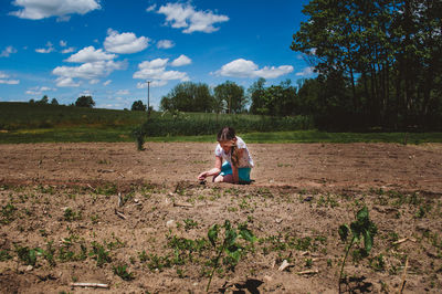 Girl kneeling on field against sky