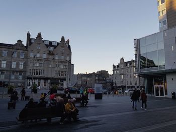 People on city street amidst buildings against clear sky