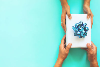 Close-up of hand giving gift box with ribbon to person against turquoise background
