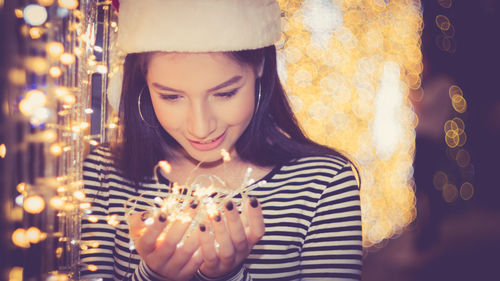 Young woman holding illuminated string lights during christmas