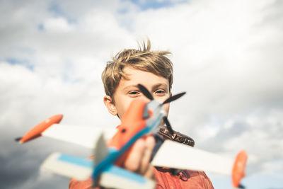 Portrait of boy playing with toy airplane against sky