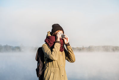 Young woman photographing from camera against sky