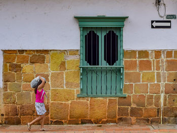 Rear view of woman walking on footpath by building