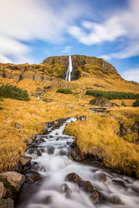 Stream flowing through rocks against sky