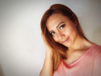 Close-up portrait of young woman smiling while standing by white wall