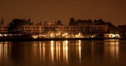 Illuminated building by lake against sky at night