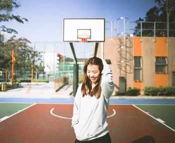 Smiling young woman standing against basketball court