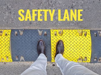 Low section of person standing on yellow arrow sign on street