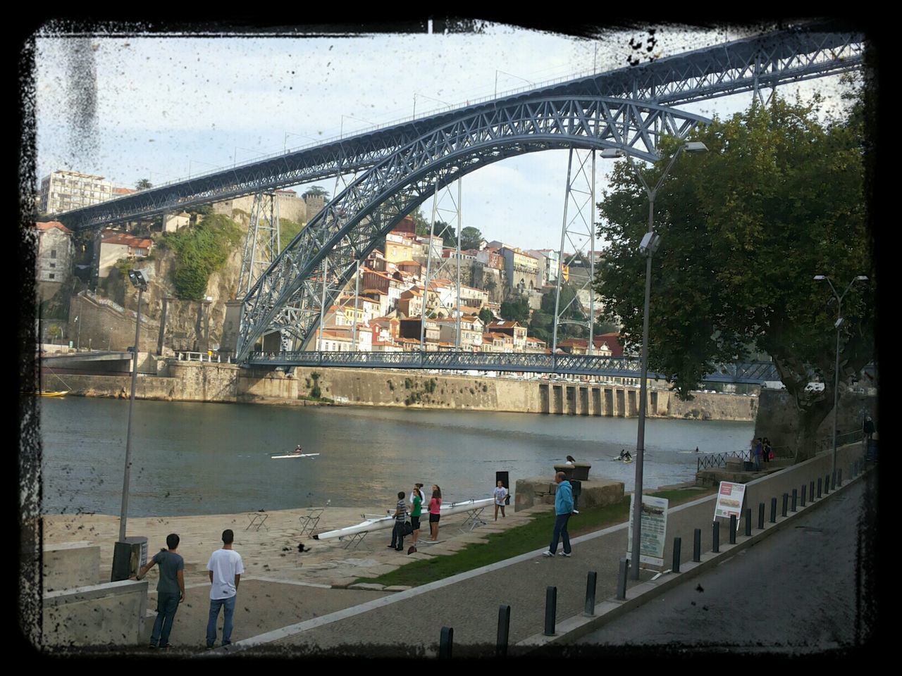 architecture, built structure, transfer print, building exterior, auto post production filter, city, men, large group of people, river, person, lifestyles, water, tree, bridge - man made structure, leisure activity, city life, walking, railing, sky