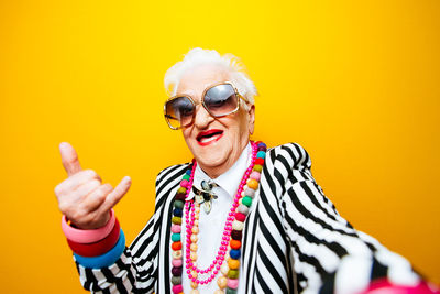 Portrait of happy senior woman gesturing against yellow background