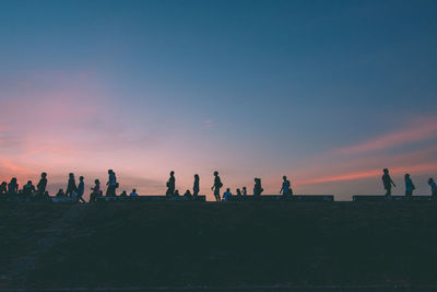 Silhouette people on land against sky during sunset