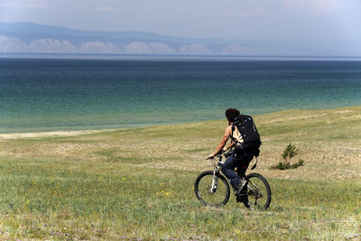 Man cycling on field against river