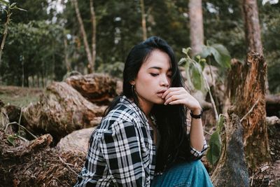 Young woman looking away while sitting on land in forest