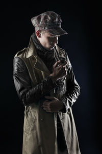 Young man smoking pipe while standing against black background