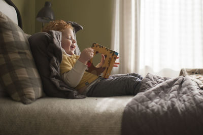 Little boy happily looks through picture book at home on his bed