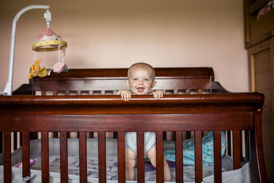 Portrait of happy baby girl standing in crib against wall