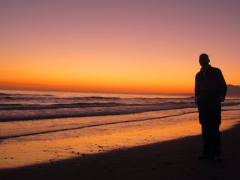 Silhouette man standing on beach against sky during sunset