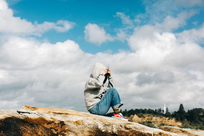 Man sitting on rock against sky