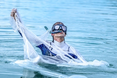 Mature man wearing scuba mask tearing plastic in sea