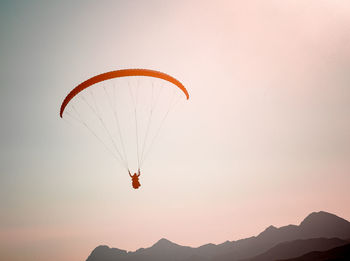 Low angle view of man paragliding against clear sky during sunset