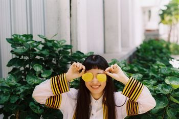 Smiling young woman holding leaves while standing against plants