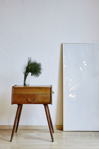 Potted plant on drawer with picture frame by wall