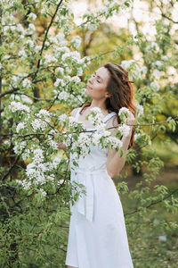 A cute happy young woman with a hairstyle in a white dress is walking enjoying nature in the summer