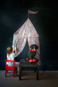 Kid with dog poodle draw circus tent on black chalk board, children's creativity and imagination