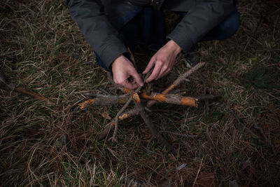 Cropped image of person arranging wooden sticks over grass field