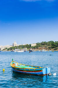 Boats moored in sea against clear blue sky